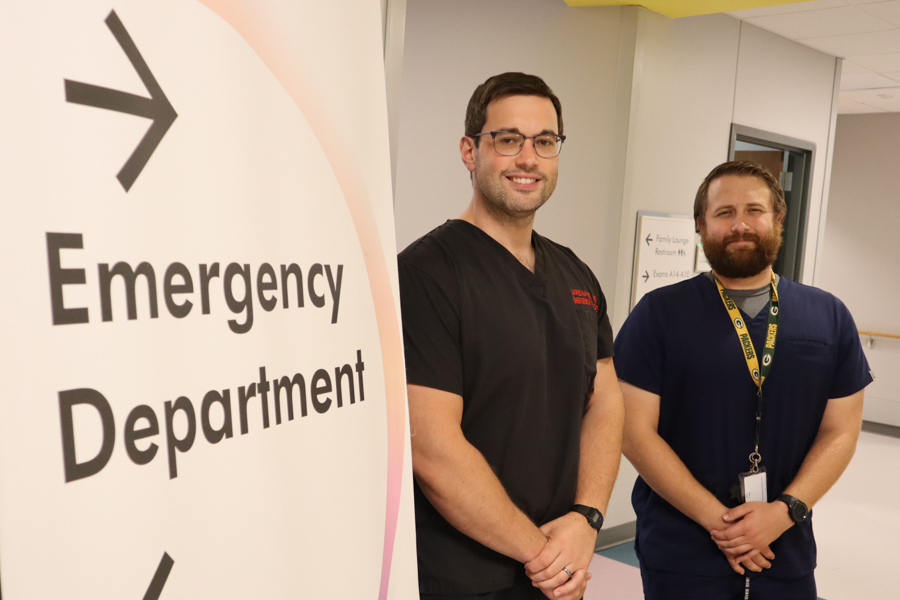 two male physicians in scrubs standing next to an Emergency Department sign