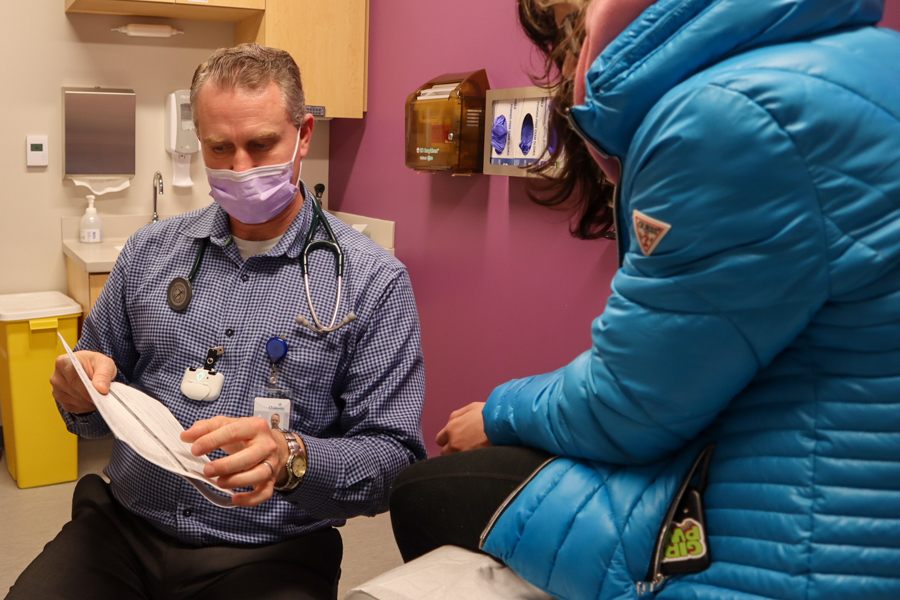 Doctor shows paperwork to adolescent patient in doctor's office.
