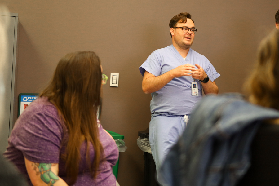 a man in scrubs talks in the back of the room while people watch