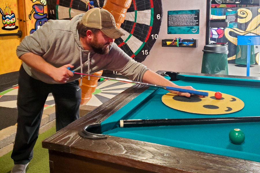 man plays billiards with a golf ball and golf club