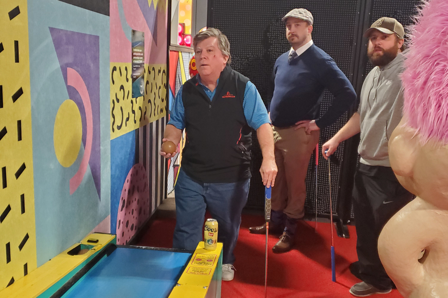 man plays skee-ball in front of two men watching him