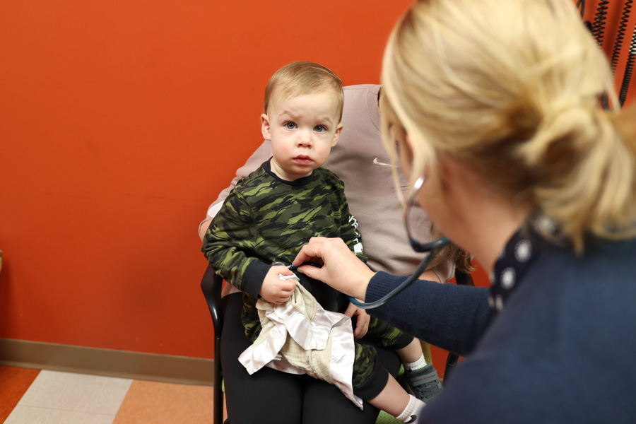 child sits on mom's lap while doctor listens to his heart