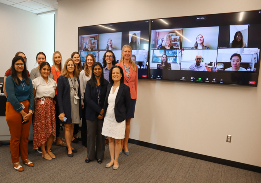 group of researchers standing in front of a video screen with people on it