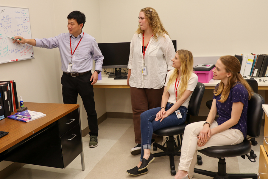 researcher writes something on white board as lab team watches