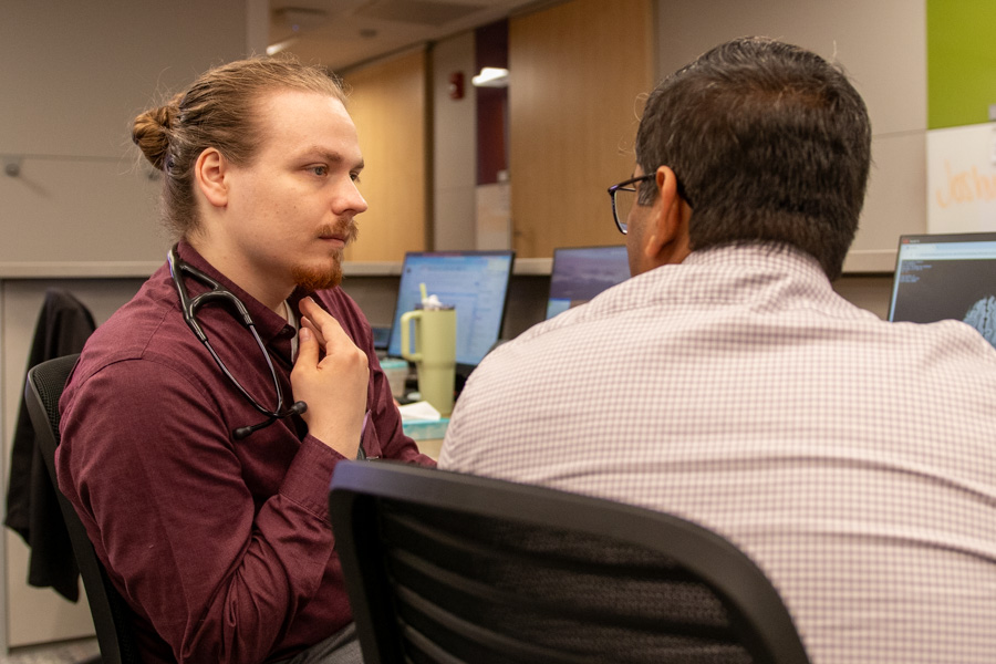 two men talk sitting at desk in medical office