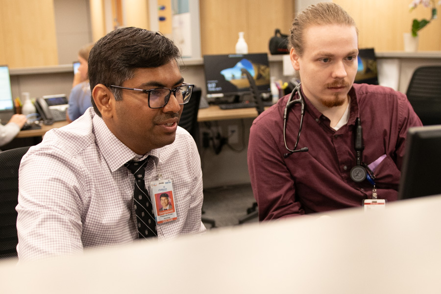 Two men sit at a desk looking at a computer