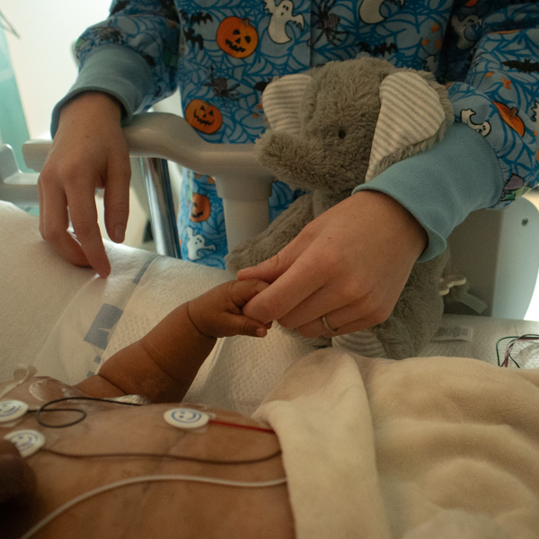 baby holding hand of adult in hospital bed