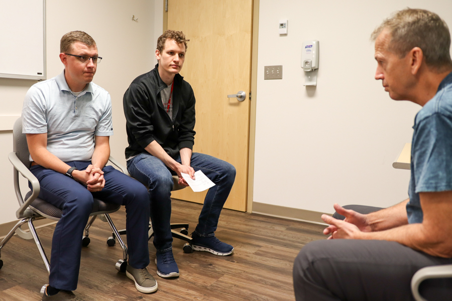 two men seated in chairs talk to another man in a chair