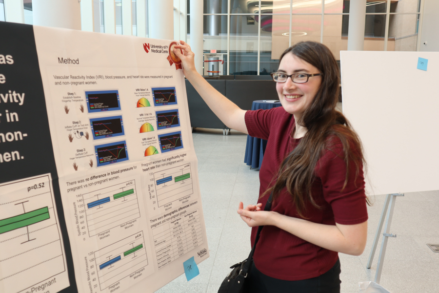 student hanging up poster and smiling at camera