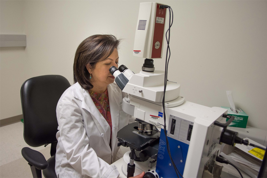 A woman in a white coat looks through a microscope