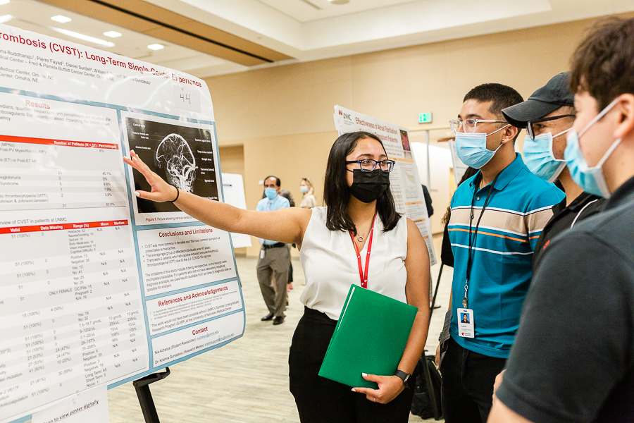 An undergraduate student explains a research poster to two observers