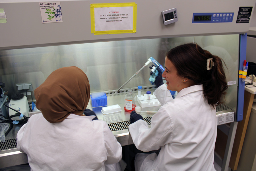 Two researchers in white coats work side-by-side in a lab