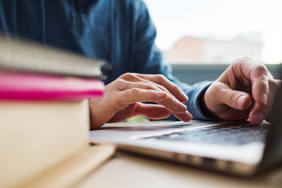 Person typing on laptop with books next to them