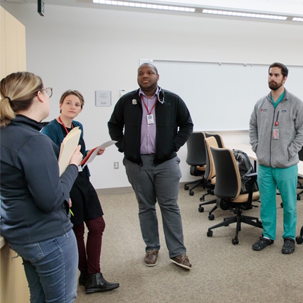 PhD students standing in a circle listening to a teacher