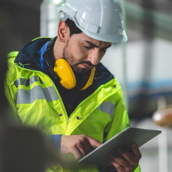 A man in a hard hat and a vest looking at a clipboard.