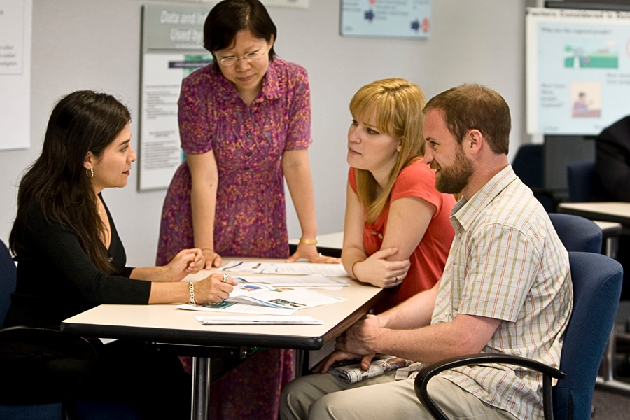 Three students around a table with a teacher discussing documents