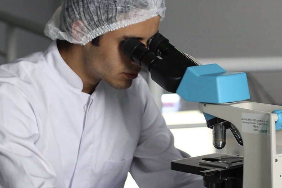 A man in a lab looking through a microscope.