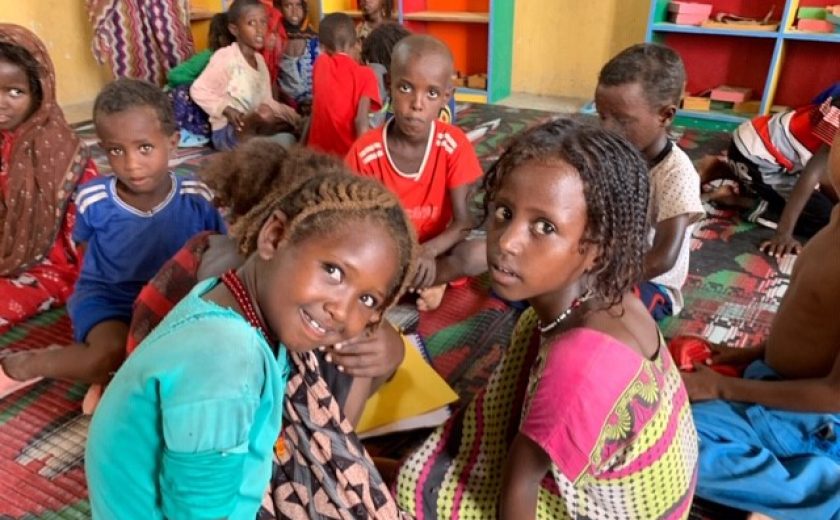 Image of children from Ethiopia sitting on the floor in a classroom in colorful clothing.