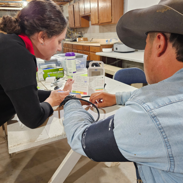 A woman is taking the blood pressure of a man wearing a cowboy hat.