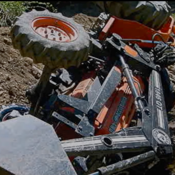 An orange tractor with bucket loader that is overturned in dirt.