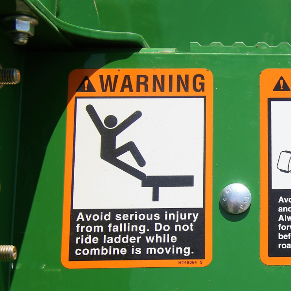 Picture of warning sticker on a green tractor that depicts a person falling and says "Avoid serious injury from falling. Do not ride ladder while combine is moving."