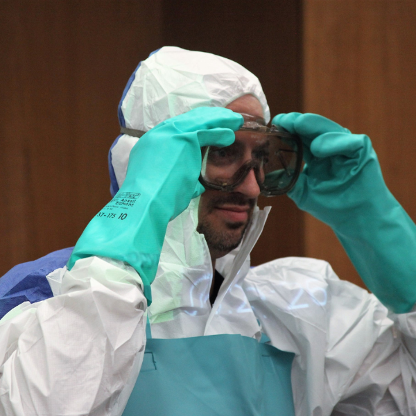 A man wearing white disposable coveralls, chemical protective gloves, and goggles. 