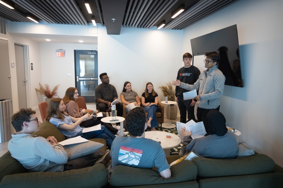 two students present to a group of students seated on couches and chairs