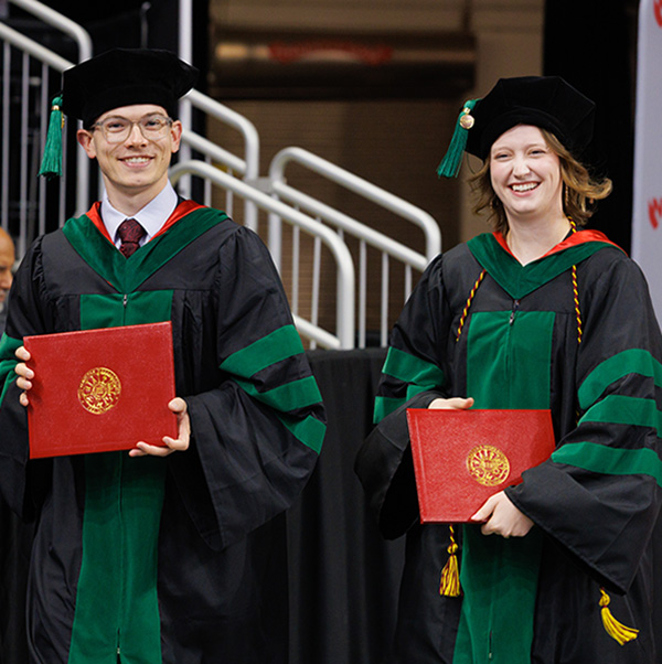 UNMC students in graduation robes holding diplomas