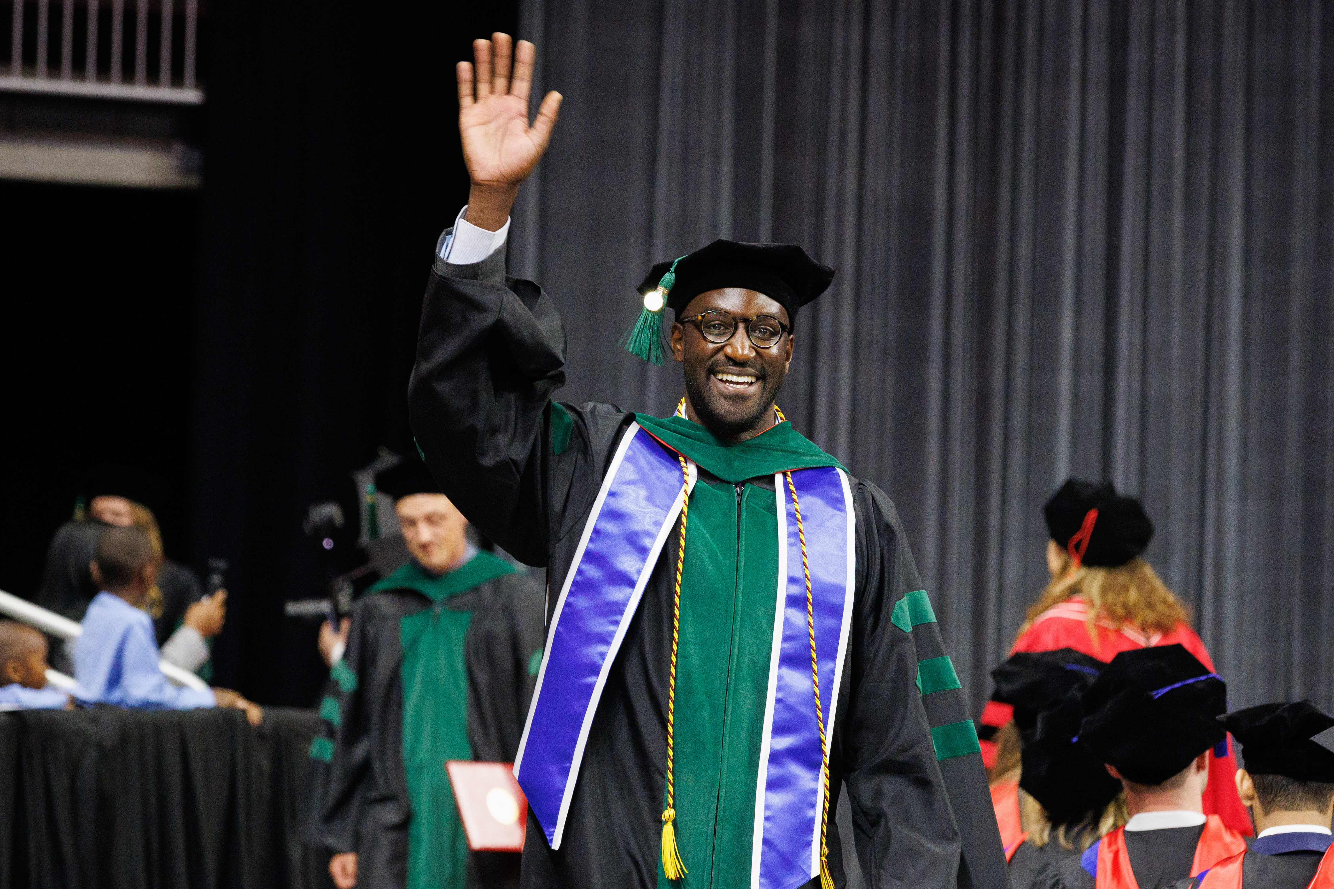 a male student waves to the crowd at the UNMC commencement ceremony