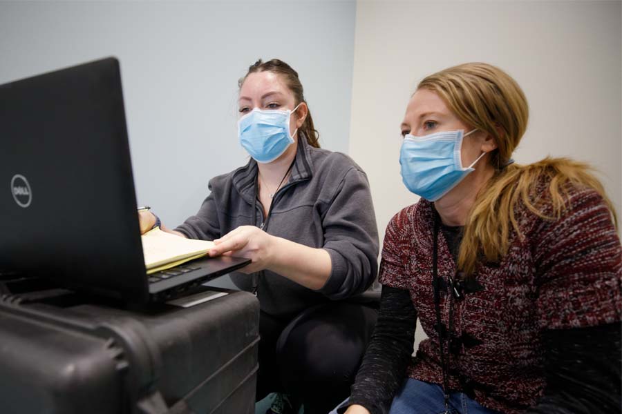 Two people with masks look at a computer screen