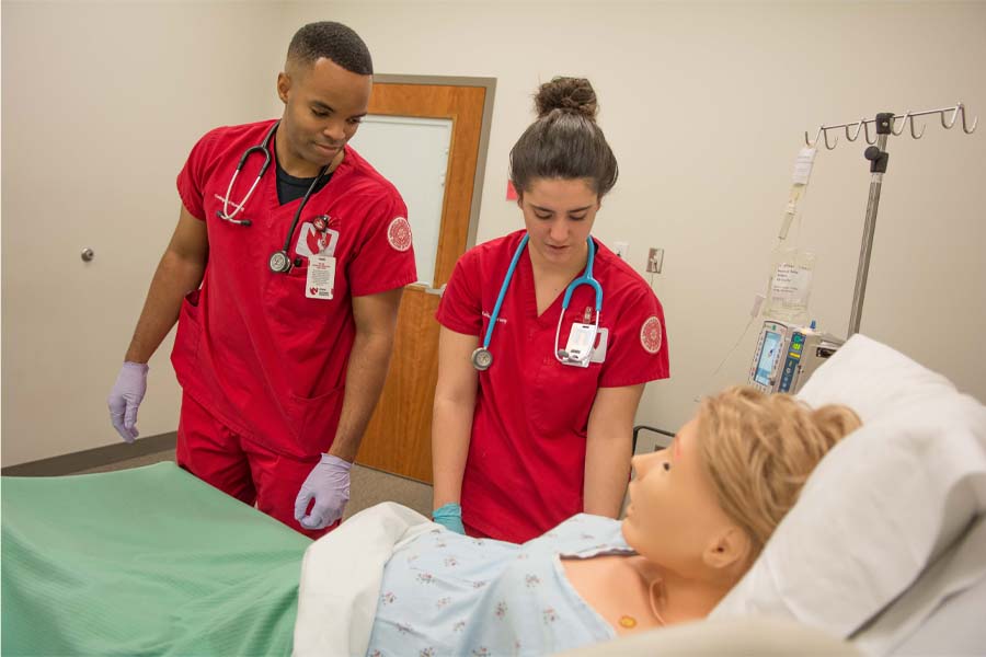 Two nursing students stand over a manikin