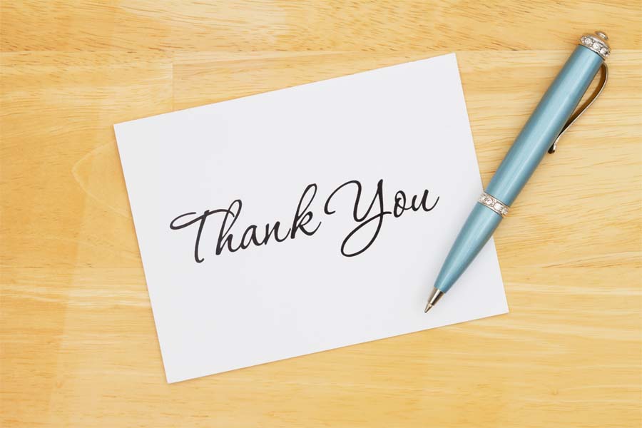 A piece of paper with the words "Thank You" and a pen sit on a table