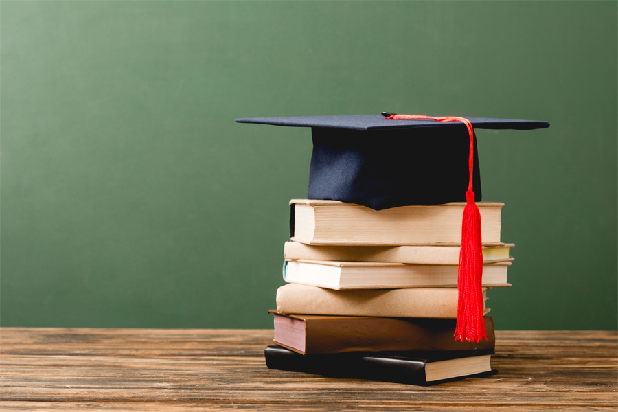 A stack of books with a graduation cap on top against a green background