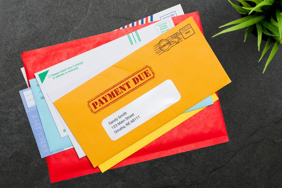 stack of mail, envelope with payment due stamp, plant on a wooden desktop