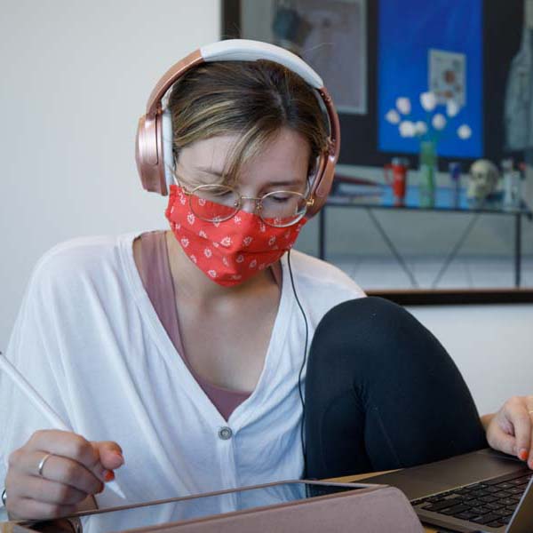 A woman in a mask studies at a laptop