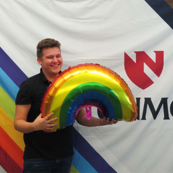 A male student holds a rainbow helium balloon