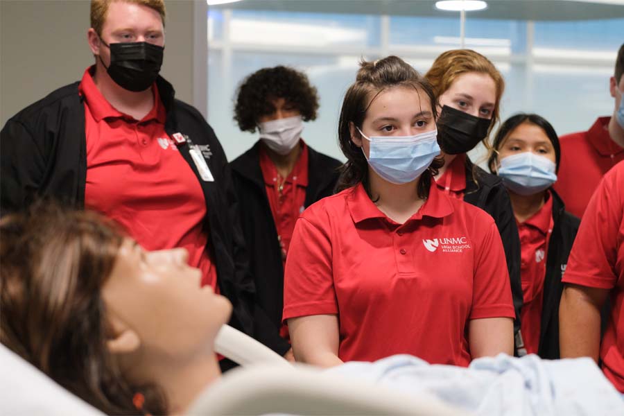A group of UNMC High School Alliance students stand behind a mannequin in a hospital bed