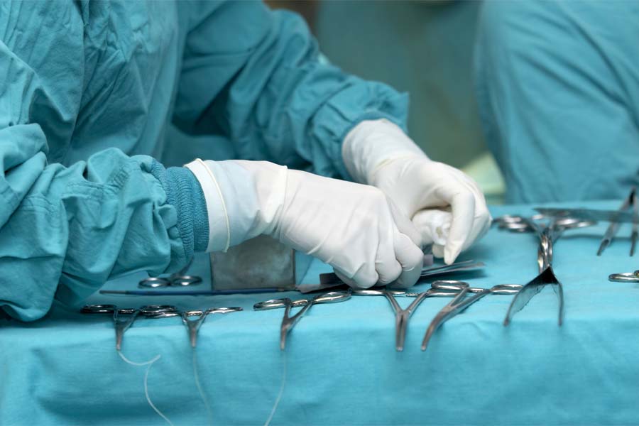 A pair of gloved hands reach for surgery tools
