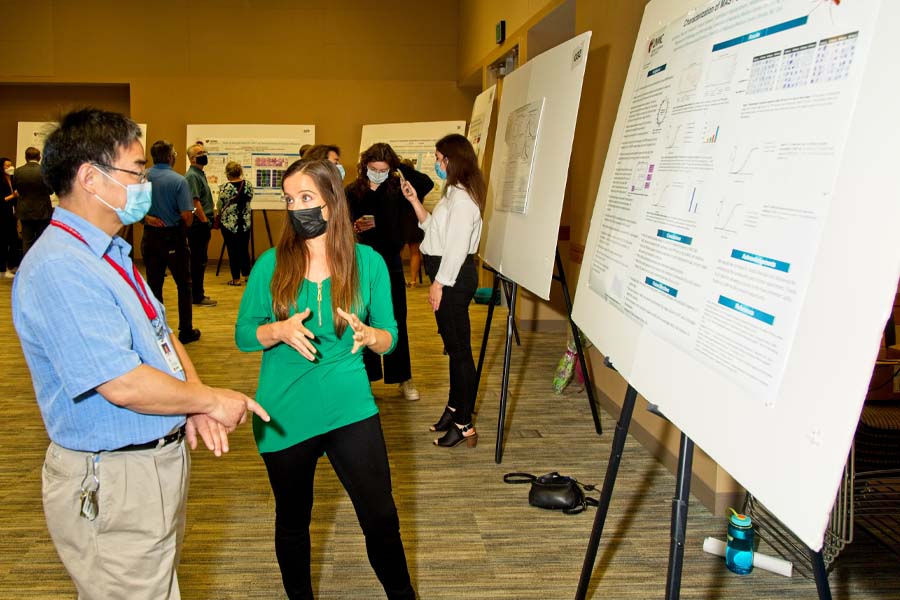 A student stands in front of a poster presentation of her research