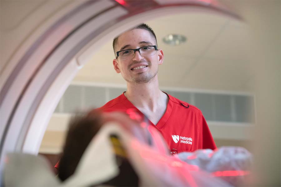 A man in red scrubs stands behind an MRI machine