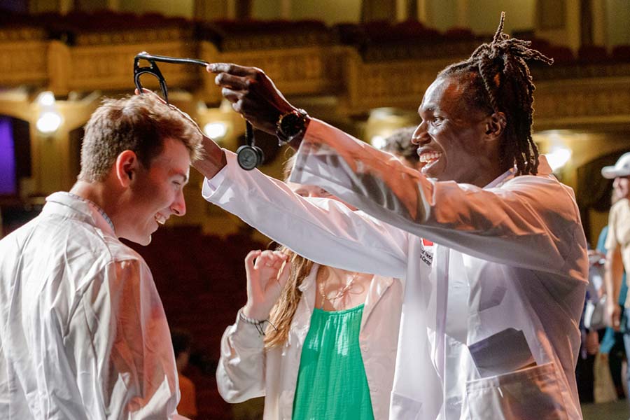 A student presents a stethoscope to a new medical student to a white coat ceremony in the UNMC College of Medicine.