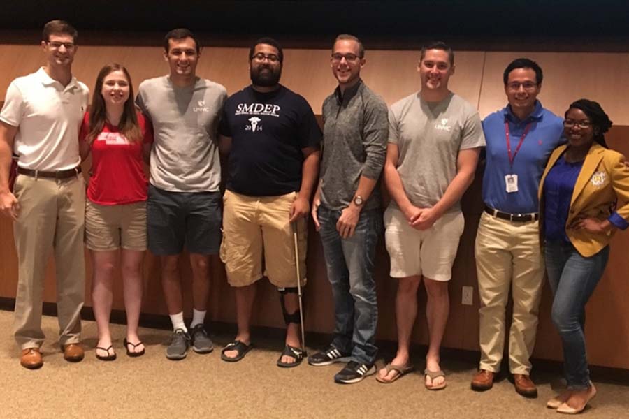 Eight people pose in front of a stage