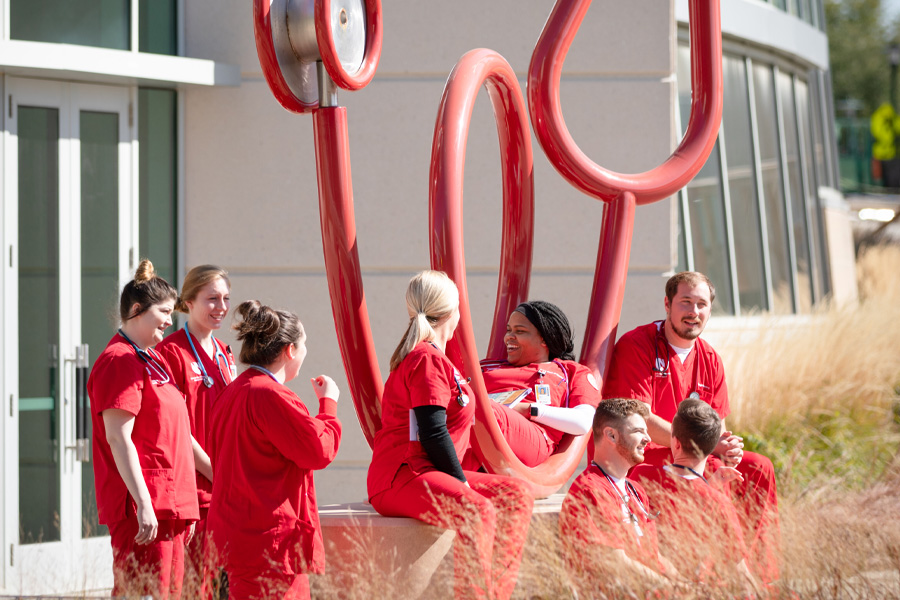 Eight nursing students sit near a sculpture of a stethoscope