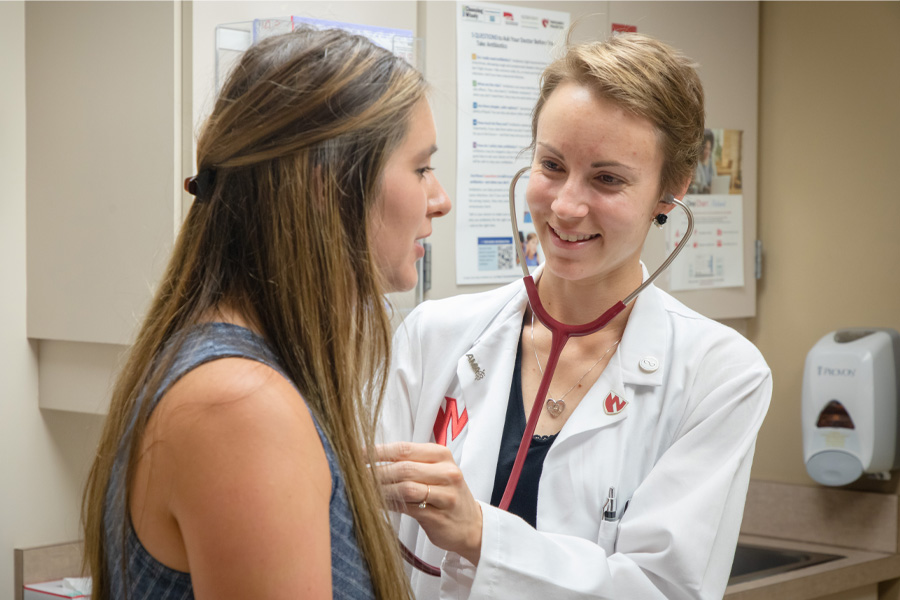 A doctor in a white coat listens to a patient's heartbeat