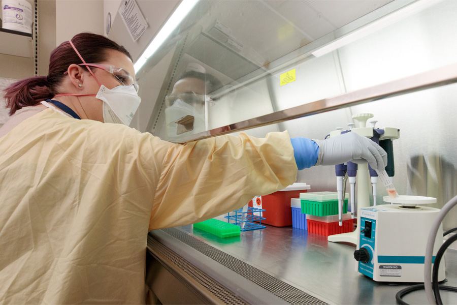 A woman wearing a mask and protective plastic sheeting works in a lab