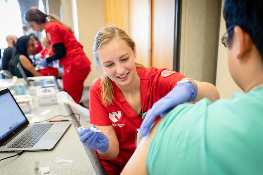 A student wearing red scrubs prepares to administer a flu vaccine