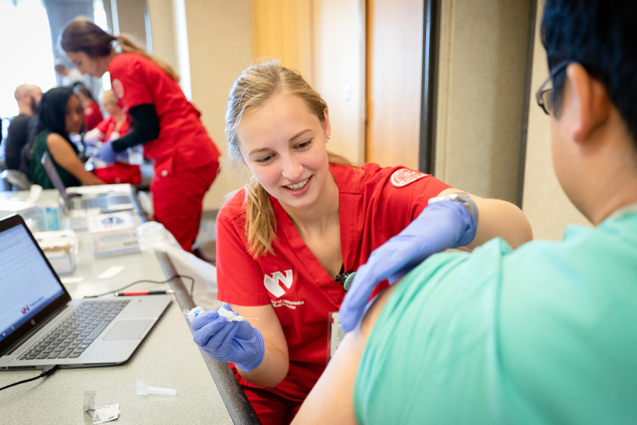 A student wearing red scrubs prepares to administer a flu vaccine