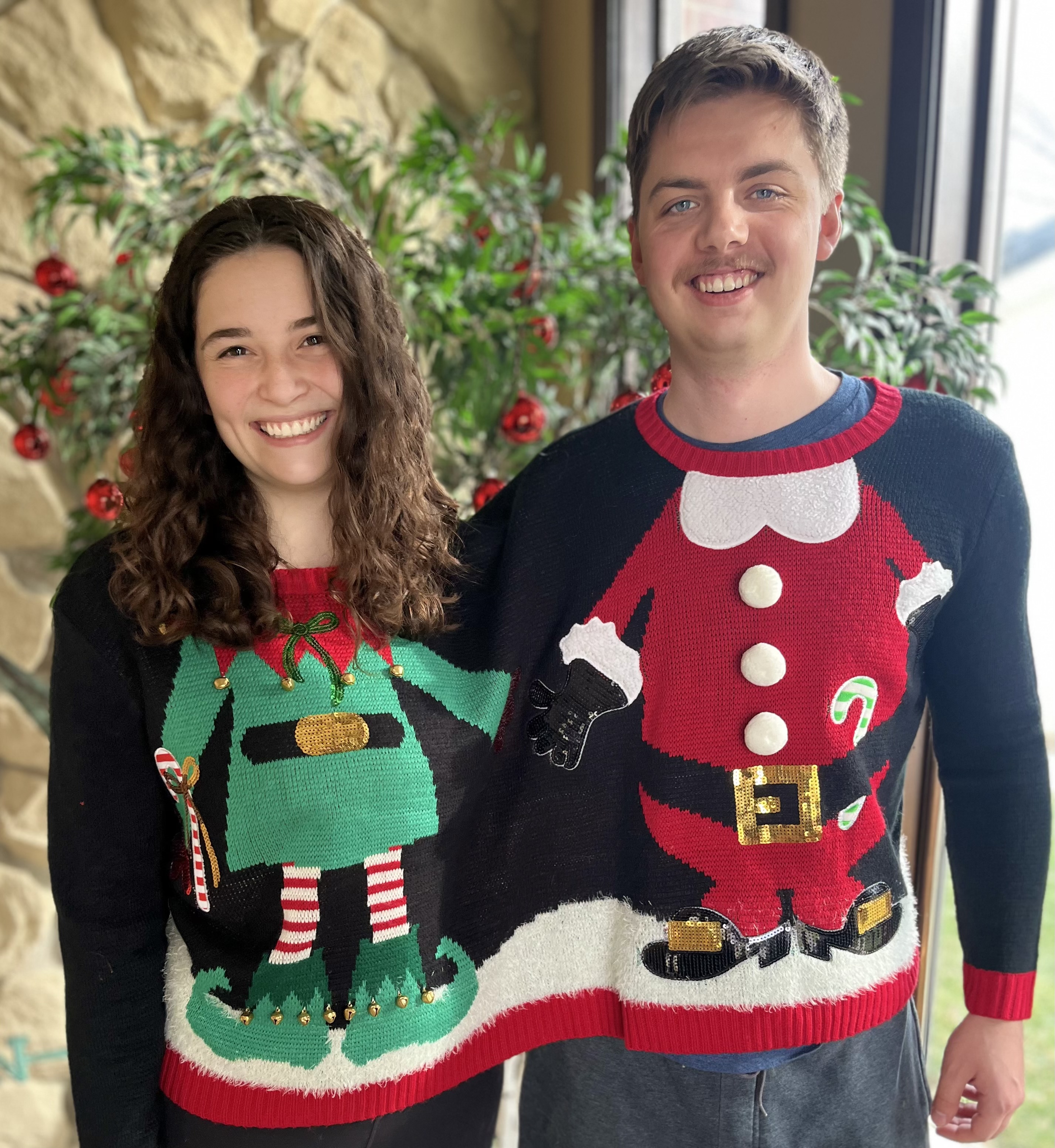 Student and friend wearing a sweater with two necks - one with head above an elf body, the other above a Santa body. They are holding hands.