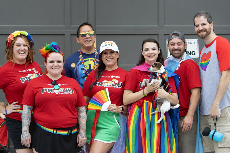 A group of seven people wearing pride shirts and rainbow attire