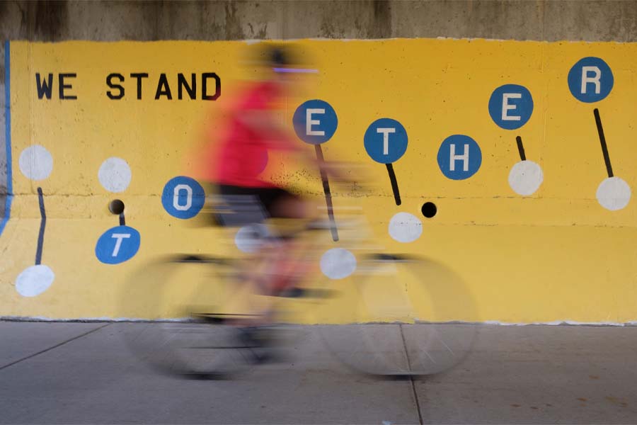 A biker rides past a mural with the phrase "We stand together"